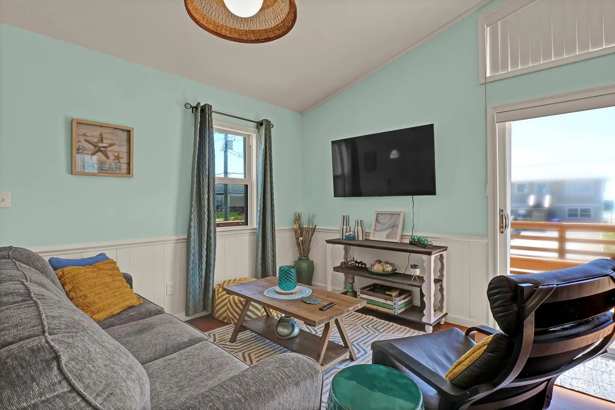 A cozy, pet-friendly living room with a comfortable sofa, coffee table, television, and a window letting in natural light. The space feels relaxing and open, inviting both people and pets to unwind after time at the beach.