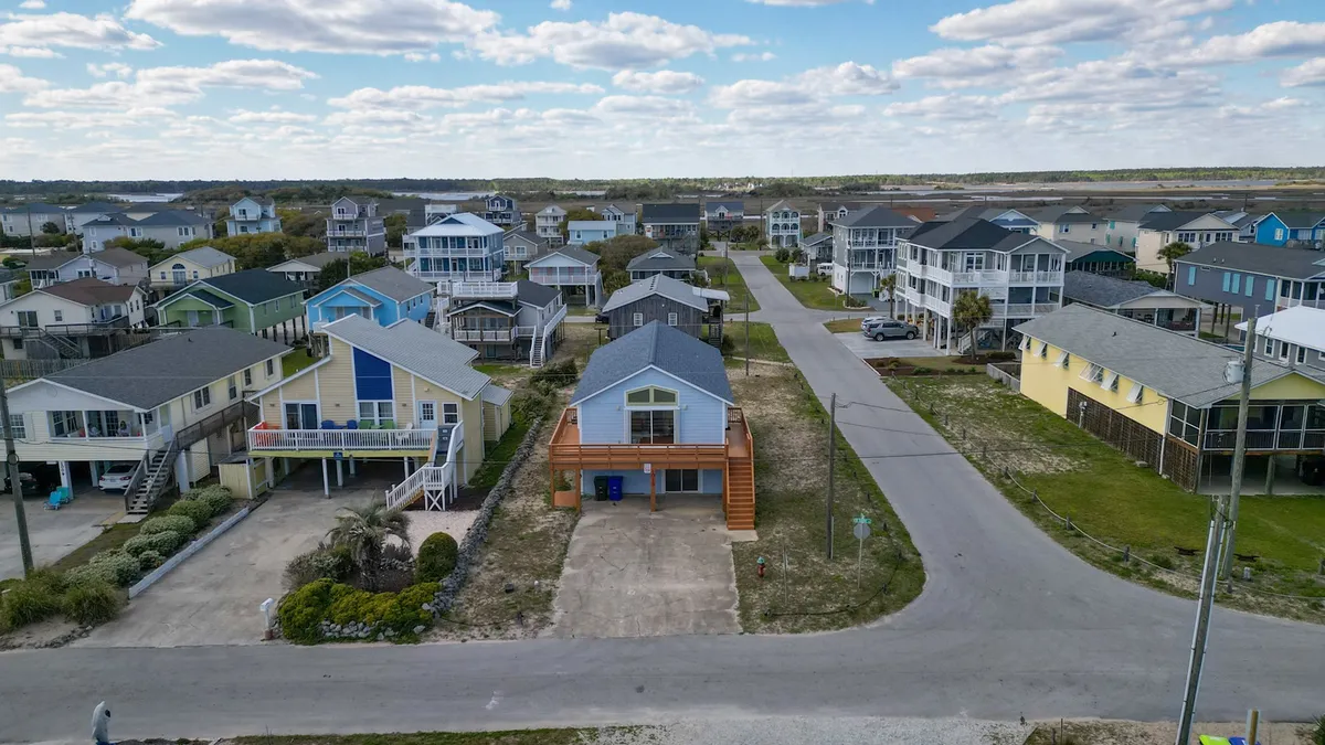 A landscape-oriented view of a quiet neighborhood with colorful houses, a wide street, and inviting sidewalks. The scene feels relaxed and family-friendly, ideal for casual walks, bike rides, or taking the dog out for a stroll.