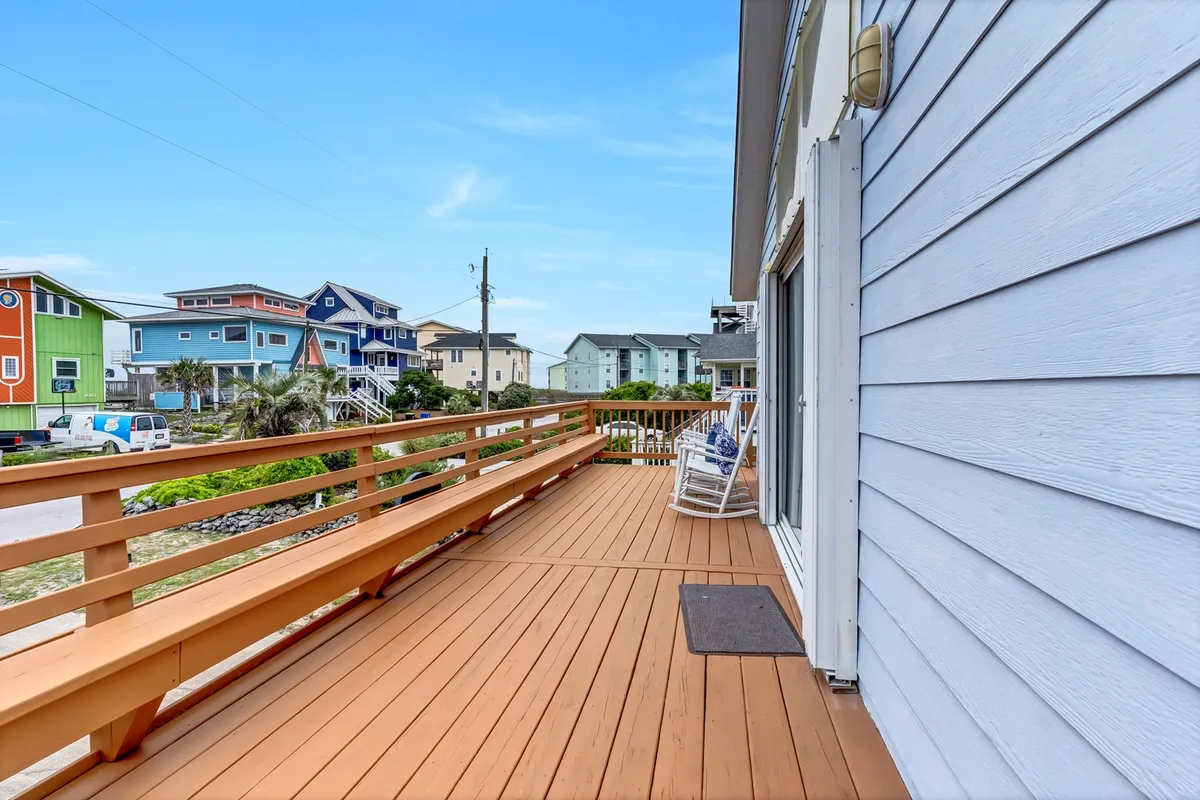 A charming exterior deck scene with a railing, a rocking chair for relaxing, and a backdrop of neighboring colorful houses. The setting is cheerful and perfect for socializing or unwinding after a day out.
