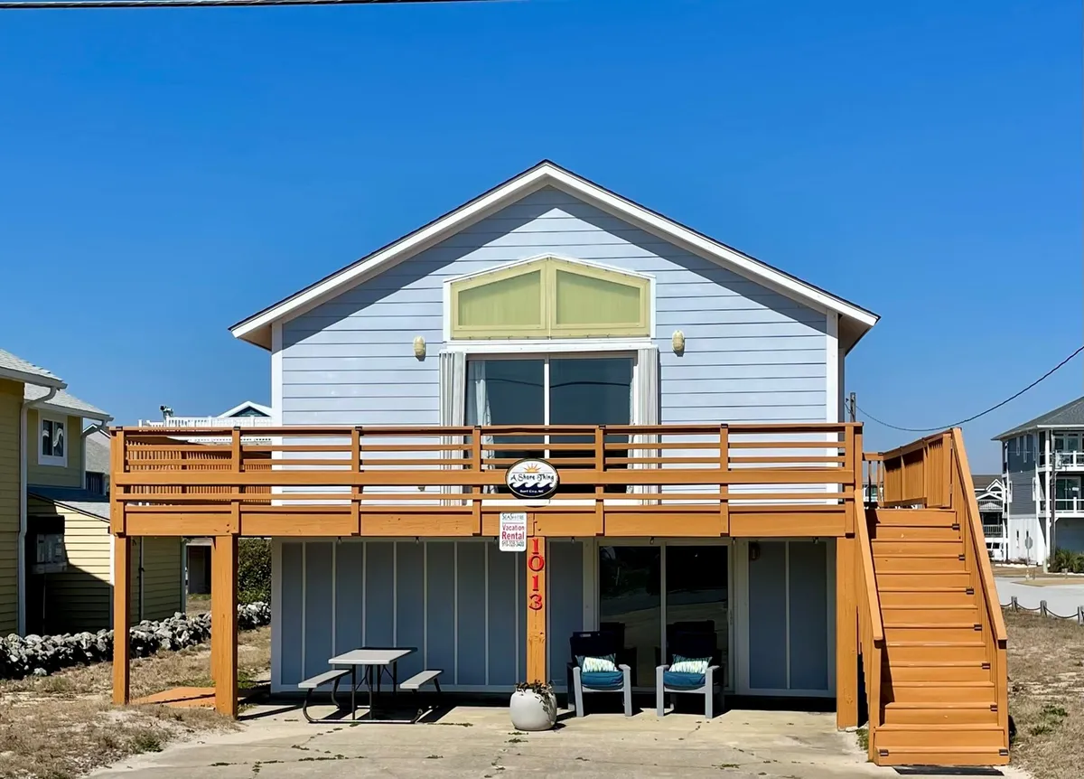 This image captures the exterior deck with a welcoming railing, large windows offering glimpses into the home, and a staircase leading up. The deck is an inviting space for guests to relax, socialize, or enjoy views, hinting at the lively atmosphere just beyond.