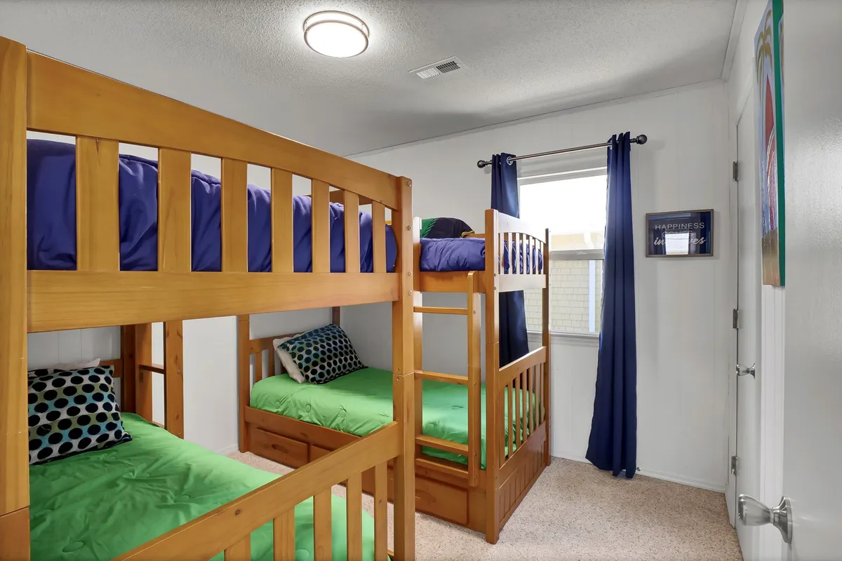A bright, playful bunk room with colorful bedding and a window letting in natural light. The space feels lively and cozy, perfect for children to unwind, play, and share stories after a day at the beach.