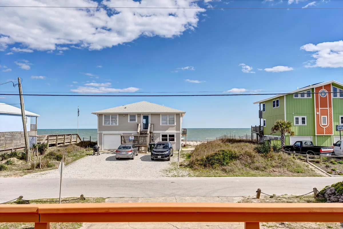 A vibrant exterior shot featuring a wide beach view, colorful houses, and cars parked in the driveway. The open street and sandy shoreline evoke a sense of accessibility and adventure, perfect for walks with pets or family outings.