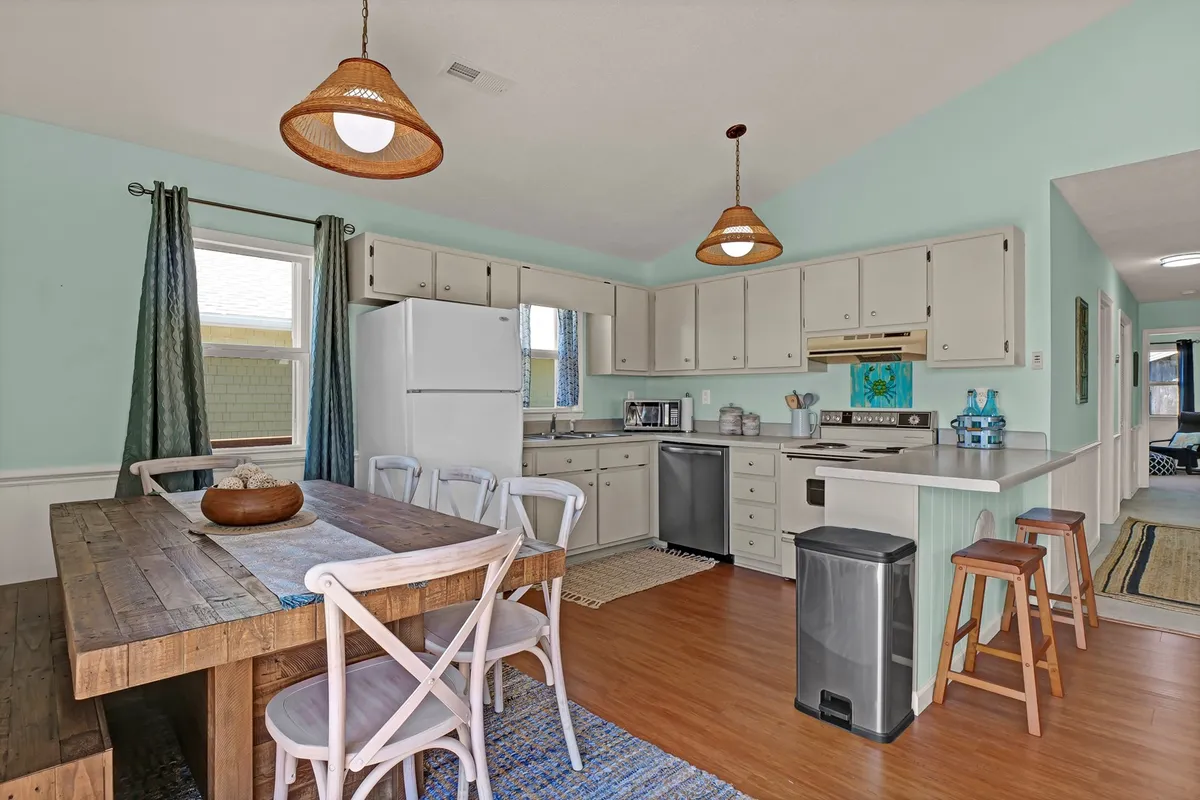 A warm, welcoming view of the open-plan interior, showing the kitchen countertop with appliances and a dining table adjacent to a window. The setting is staged for cooking and social gatherings, with clean lines and a lived-in feel that encourages both meal prep and family connection.