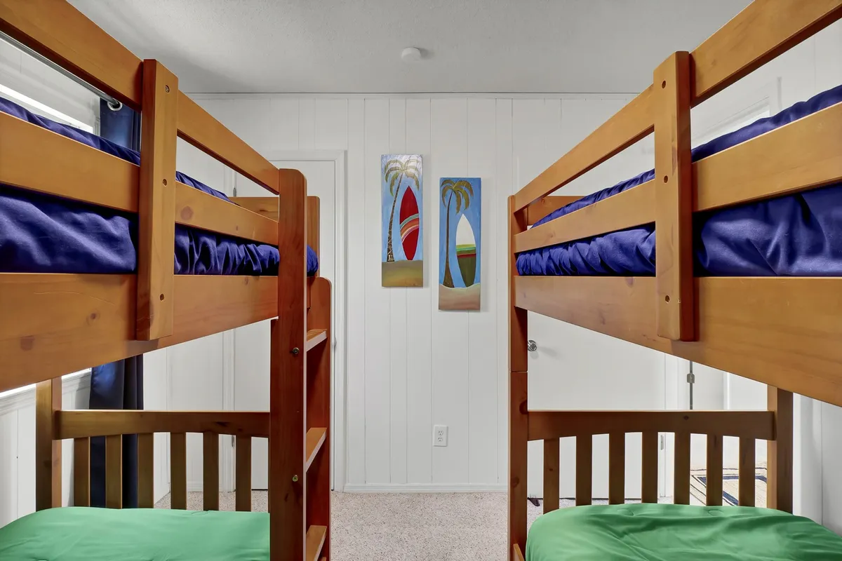 A cheerful, kid-friendly bedroom with brightly colored bunk beds, playful green bedding, and lively artwork. The room is clearly designed for children, encouraging fun, play, and cozy sleepovers.