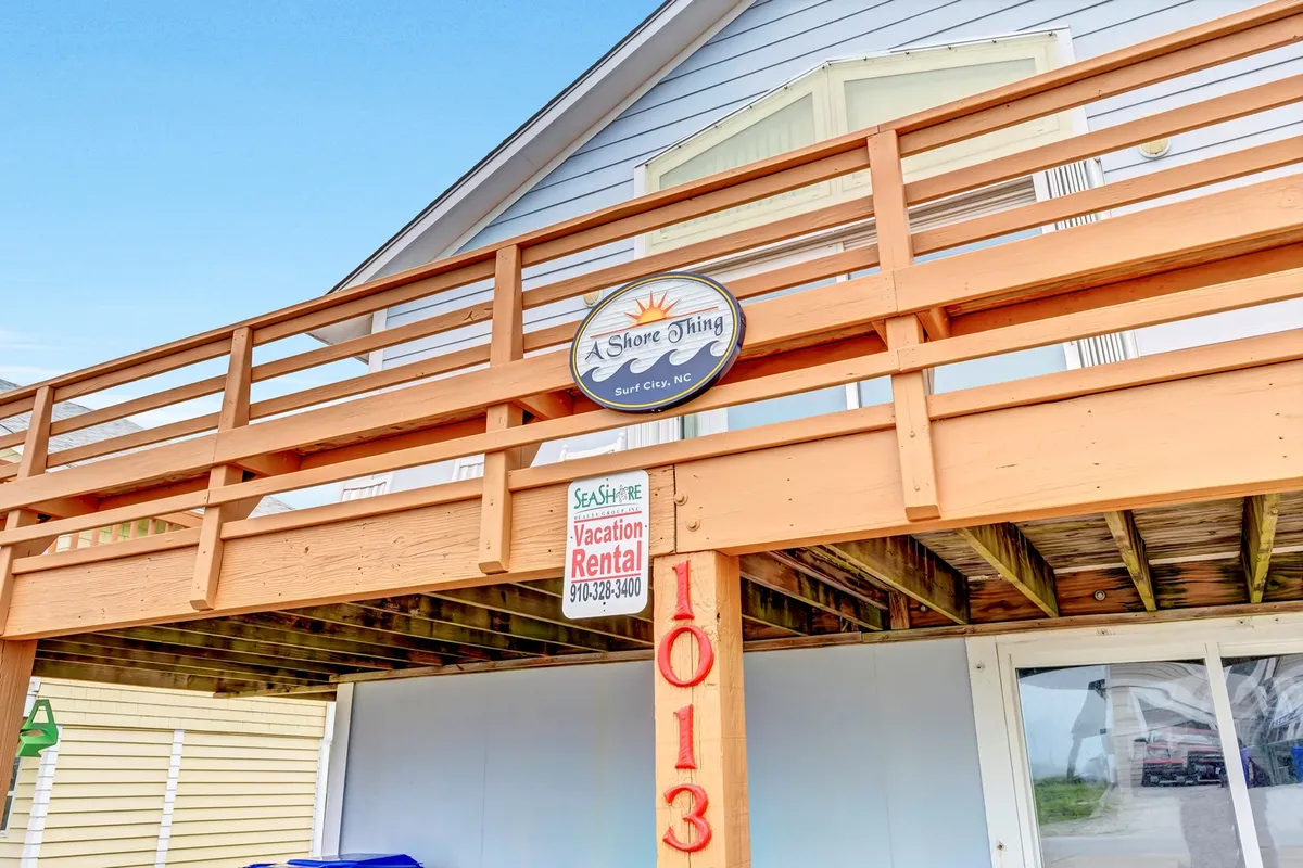 A welcoming exterior view of the home’s wooden deck, with clear signage that identifies the vacation rental. The deck looks ready for families and pets to gather before or after their beach adventure, and the proximity to the beach is hinted at by the open, airy feel and visible pathways.